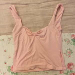 Rosa topp - Säljer en söt rosa topp i mjukt material. Perfekt för sommardagar eller som ett lager under en kofta. Toppen har en enkel design med en lätt rynkning vid bysten för extra stil. Passar bra till både jeans och kjol!