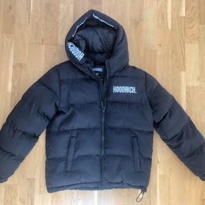 Svart pufferjacka från Hoodrich - Säljer en svart pufferjacka från Hoodrich i mycket bra skick. Jackan har en stor huva och dragkedja framtill. Perfekt för kalla dagar med sin varma och vadderade design. Den har långa ärmar och två praktiska fickor. Passar både till vardags och mer avslappnade tillfällen.