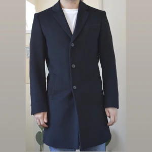 Svart kappa- Tiger of Sweden - Snygg svart kappa i ullmix från Tiger of Sweden i mycket bra skick . Modell Cempsey, strl 46. Den har en klassisk design med tre knappar framtill och en stilren krage. Passar till höst och vinter samt till både vardags och mer formella tillfällen. Använd ca tio gånger, nypris 4500:-