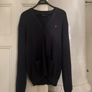 Mörkblå kofta från Ralph Lauren - Säljer en stilren mörklblå kofta från Ralph Lauren i 100% pima bomull. Den har en klassisk v-ringning och två praktiska fickor framtill. Perfekt för både vardag och fest! 