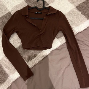 Zara topp brun, s - En brun, figursydd topp med långa ärmar och en krage. Toppen är tillverkad i ett mjukt och stretchigt material.
