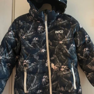Blommig vinterjacka från WA - Säljer en snygg och varm vinterjacka från WA med blommigt mönster. Jackan har en dragkedja framtill och är perfekt för kalla dagar. Den är långärmad och har en mysig huva. Perfekt för vinterns äventyr! 🌸