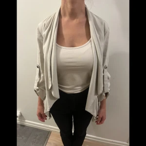 Beige kavaj med knytband - Säljer en stilren beige kavaj med knytband i midjan. Den har trekvartsärmar och en lös passform som ger en avslappnad look. Perfekt för vår och sommar, och funkar både till vardags och fest. Kavajen är i mycket bra skick och är superbekväm att ha på sig.