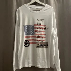 Vit långärmad tröja med tryck USA flag. y2k streetwear opium rap swag  - Säljer en vit långärmad tröja med ett unikt tryck av en amerikansk flagga .Tröjan har även en 18+ symbol och ett motiv som liknar en sedel. Perfekt för dig som vill ha något annorlunda i garderoben. 