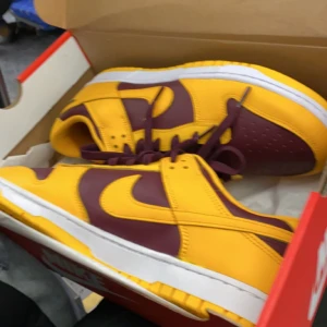 Nike Dunk Low 'Goldenrod' - Snygga Nike Dunk Low sneakers i färgerna gul och svart. Skorna har en klassisk design med snörning och en vit mellansula. Perfekta för dig som vill ha en stilren och sportig look. Skorna är lite mer använda än på första bilden. Om intresserad skriv till mig så skickar jag bild på dem!