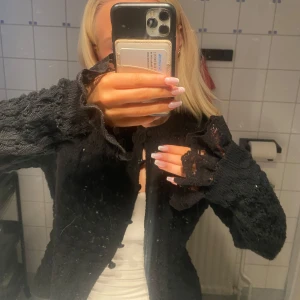 Svart stickad kofta från Zara. - Säljer en svart stickad kofta från Zara med ett snyggt hålmönster och spets detaljer. Koftan har långa ärmar och en croppad passform, perfekt för lager-på-lager-stil. Den är både stilren och bekväm, idealisk för kyligare dagar.