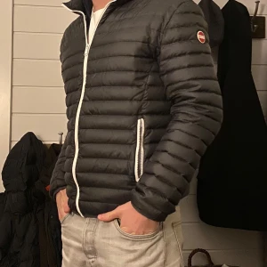 Colmar jacka - Säljer en stilren svart pufferjacka från Colmar med vit dragkedja och logga på ärmen. Jackan har en quiltad design och är perfekt för kyligare dagar. Den är långärmad och har en modern passform.