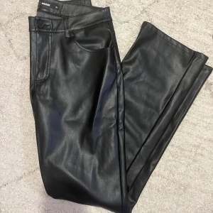 Svarta skinnbyxor från Bik Bok - Snygga svarta skinnbyxor från Bik Bok i storlek 40. Byxorna har en klassisk design med knappar och dragkedja framtill. Perfekta för en stilren look.