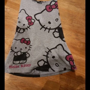 Grå Hello Kitty klänning - Sött grått linne med stort Hello Kitty-tryck i svart och rosa. Knappt använd i stlk S
