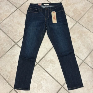 Levi's 711 Skinny Jeans - Snygga Levi's 711 Skinny jeans i mörkblå denim. Dessa jeans har en tight passform och är perfekta för en stilren look. Klassisk femficksdesign med knapp och dragkedja framtill. 30 x 30. Mid rise och helt NYA! 