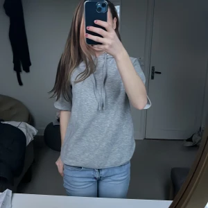 Grå hoodie med korta ärmar - Säljer en stilren grå hoodie med korta ärmar och dragsko i huvan. Perfekt för en avslappnad look. Passar bra till jeans eller leggings. Jag klippte armarna själv så det är inte sytt, men det är inget som man märker av🤍🤍