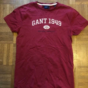 Röd t-shirt från GANT - Snygg röd t-shirt från GANT med tryck 'GANT 1949' på bröstet. Perfekt för en avslappnad stil. Kortärmad och tillverkad i mjukt material för extra komfort. Tröjan är i gott skick👍