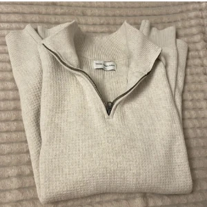 Beige half zip tröja  - Säljer en stilren beige half zip tröja från THESE GLORY DAYS. Tröjan har en praktisk dragkedja vid halsen och långa ärmar. Perfekt för kyligare dagar.