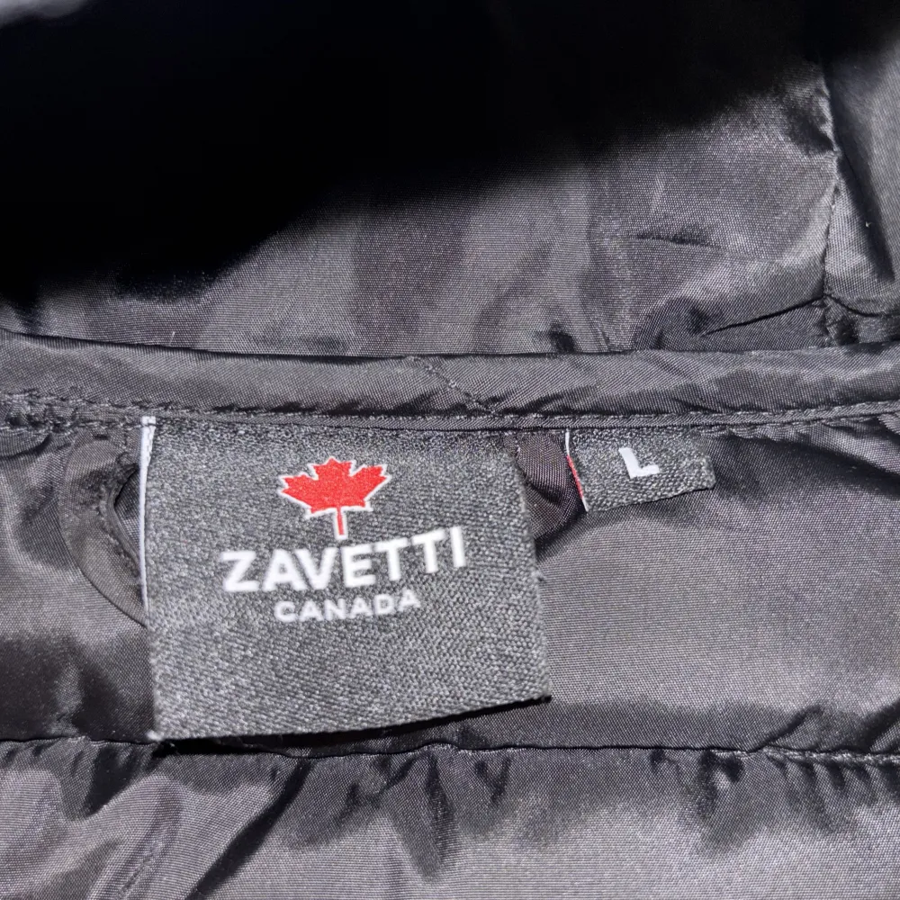 Snygg svart cardigan från Zavetti Canada med huva och dragkedja. Jackan har ett stilrent märke på bröstet och är perfekt för kyligare dagar. Den är både funktionell och trendig med sin quiltade design.. Takit.