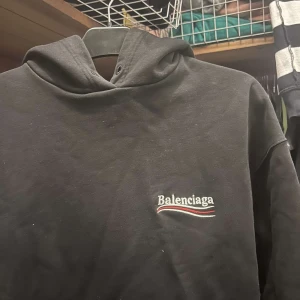 Svart hoodie från Balenciaga - Säljer en stilren svart hoodie från Balenciaga med logotyp på bröstet. Perfekt för en avslappnad och trendig look.