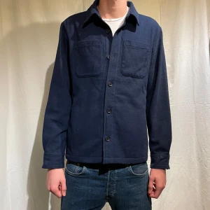 Mörkblå overshirt - Snygg mörkblå overshirt från med knappar framtill och två bröstfickor. Perfekt för lager-på-lager-stil. Den har långa ärmar och en klassisk krage. Minimalistiskt märke på ärmen. Knappt använd, Nypris:1499kr, modellen är 186cm