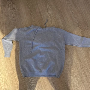 Grå hoodie - Säljer en stilren grå hoodie med dragsko i huvan. Perfekt för en avslappnad look. Den har långa ärmar och ribbade muddar vid ärmslut och nederkant.