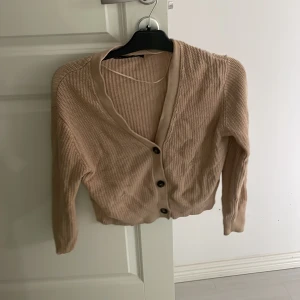 Beige ribbad kofta - Säljer en beige ribbad kofta med knappar framtill. Koftan har en v-ringad design och långa ärmar, perfekt för lager på lager-stil. Passar bra till både jeans och kjol. Den ser skrynklig ut för den legat i en låda i mitt rum länge. Annars fin!
