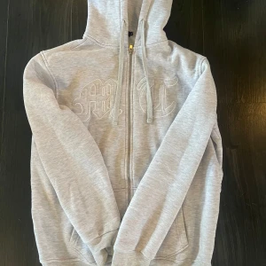 Tuttolente hoodie - Säljer en grå hoodie tuttolente med dragkedja och huva. Den har ett broderat mönster på framsidan och ett tryck av en örn på baksidan. Perfekt för en avslappnad stil.