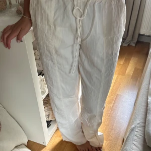 Vita byxor med snörning - Snygga vita byxor med elastisk midja och snörning för en bekväm passform. Byxorna har en avslappnad stil med fickor bak, perfekta för en casual look.