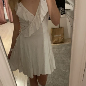 Vit omlottklänning med volang - Charmig vit miniklänning med omlott och volangdetaljer.