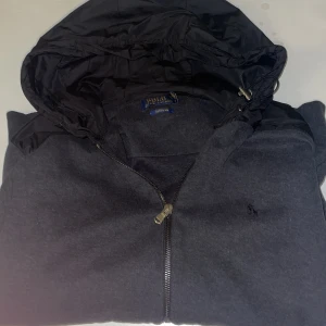 Polo Ralph Lauren cardigan - Säljer en stilren cardigan från Polo Ralph Lauren med dragkedja och huva. Perfekt för en avslappnad look. Den har en diskret logga på bröstet.