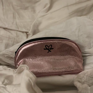 Rosa glittrig necessär från Victoria's Secret - Snygg rosa glittrig necessär från Victoria's Secret med dragkedja och ett hjärtmotiv på framsidan. Perfekt för att förvara smink eller andra småsaker. Inuti finns en etikett med texten 'love, Victoria'.
