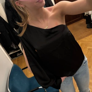 Svart oneshoulder topp - Svart oneshoulder topp med en elegant design. Perfekt för utekväll. Toppen är öppen längst med ärmen, som blir en extra detalj💕