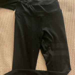 Svarta leggings från Stronger - Snygga svarta leggings från Stronger med hög midja och meshdetaljer på låret. Perfekta för träning eller en aktiv vardag. De är tillverkade i ett stretchigt material som ger en tight passform.