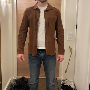 Brun mocka overshirt från Jofama x King - Säljer en snygg brun mocka overshirt från Jofama x King. Jackan har en klassisk krage och knappar framtill. Perfekt för lager-på-lager-stil och passar bra till både jeans och chinos.