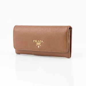 Brun plånbok från Prada - Elegant brun plånbok från Prada i skinn med guldiga detaljer. Den har en praktisk dragkedja på baksidan och det ikoniska Prada-logotypen på framsidan. Perfekt för att hålla dina kort och kontanter organiserade. 100 äkta köpt på bukowskis. 