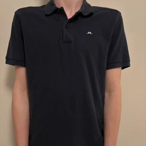 Svart pikétröja från J.Lindeberg - Snygg svart pikétröja från J.Lindeberg. Storlek S. Modellen på bilden är 178 cm.