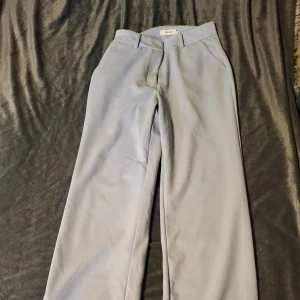 Ljusblå kostymbyxor från Reserved - Snygga ljusblå kostymbyxor från Reserved i en klassisk design. Byxorna har en rak passform och är perfekta för en stilren look. De har hällor för bälte och en diskret dragkedja framtill.