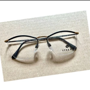 Svarta halvbågar från Vogue - Snygga och stilrena halvbågar från Vogue i svart med gulddetaljer på skalmarna. Glasögonen har en modern design med transparenta linser och justerbara näskuddar för extra komfort. Perfekta för en elegant look.