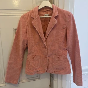 Rosa manchesterkavaj från Gina - Snygg rosa kavaj i manchester från Gina med klassisk krage och knappar framtill. Två fickor med lock ger en stilren look. 