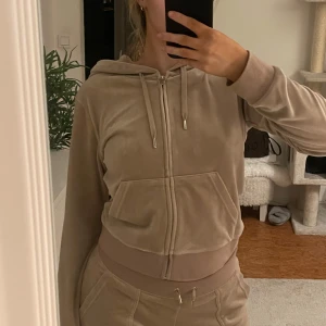 Beige kofta från Juicy Couture - Säljer en velour hoodie från Juicy Couture. Den har en dragkedja framtill och en liten logga på bröstet. Köpte när den va ”populär” och har sedan dess bara hängt i min garderob. Köpt på bubbleroom om jag inte minns fel. Storlek M, men passar även S.