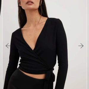 Svart omlottopp -helt ny  - Oanvänd snygg svart omlottopp med lång ärm och knytning i midjan. Toppen har en v-ringad design och är perfekt för en stilren look. Från NAKD
