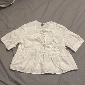 Vit blus från H&M - Säljer en söt vit blus från H&M med knytning framtill och volangdetaljer nedtill. Blusen har trekvartsärmar och en luftig passform, perfekt för vår och sommar.