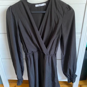 Svart omlottklänning från NA-KD - Säljer en elegant svart omlottklänning från NA-KD i storlek 34. Klänningen har långa ärmar och en smickrande v-ringad design. Perfekt för både fest och vardag! 🖤 Bandet runt om har försvunnit men fin endå