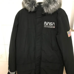 Ny Vinterjacka/ NASA st M ( 176+) - Svart vinterjacka från divided med NASA motiv.Köptes till min pappa i julklapp men han inte användas då han blev sjuk och gick bort. Ingen lapp i den pga det. Från Divided. St M men passar upp ungdomar upp till 176. Fusk päls, flagga på ärmen. 