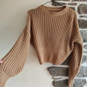 Beige stickad tröja - Säljer en superfin beige stickad tröja som är perfekt för höst och vinter. Den har en mysig och varm känsla med långa ballongärmar och en croppad passform. Materialet är 100% akryl vilket gör den både mjuk och hållbar. Perfekt att matcha med ett par jeans eller en kjol för en avslappnad look!