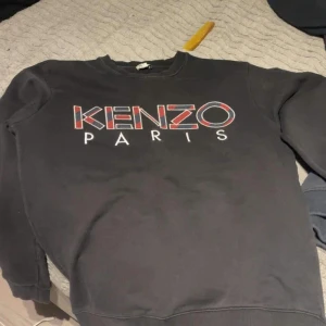 Svart sweatshirt från Kenzo - Säljer en snygg svart sweatshirt från Kenzo med deras ikoniska logga i rött och vitt på bröstet. Tröjan är långärmad och perfekt för både höst och vinter. Den är i bra skick och superbekväm att ha på sig. Passar perfekt till både jeans och joggers!