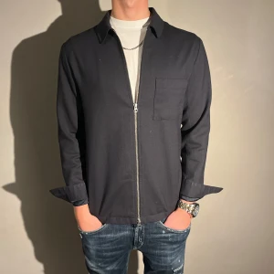 Mörkblå overshirt  med dragkedja - Riktigt snygg overshirt med dragkedja framtill. Perfekt för en stilren look till sommaren. Overshirt en har en normal passform och helt perfekt till sommar kvällarna. Enkel och stilren design som passar till många tillfällen med märket J.Lindberg. Skriv vid intresse 🤩orginalpris 2800kr