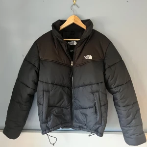 Svart dunjacka från The North Face - Säljer en svart dunjacka från The North Face. Perfekt pufferjacket för kalla dagar med sin varma och bekväma passform. Den har också praktiska fickor med dragkedja. Strl M. Skriv om det finns frågor!