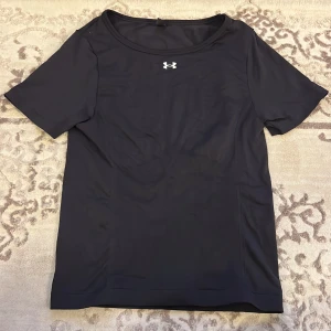 Helt ny svart träningströja från Under Armour - Säljer en helt ny svart t-shirt från Under Armour. Den är kortärmad och är perfekt för träning. Diskret logga på bröstet. Perfekt för dig som vill ha en bekväm och funktionell t-shirt för aktiva dagar. Tröjan är i storlek M och är aldrig använd men lapparna är avklippta. Köpt för 549kr. Kan tänka mig gå ner i pris vid snabb affär🫶 