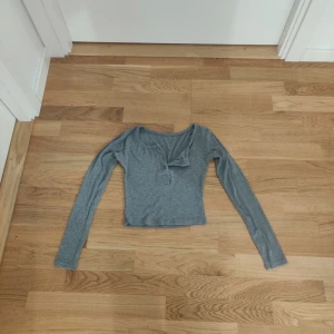 Grå långärmad topp - Grå långärmad croptopp med knappar framtill. Har en liten fläck på ena armen som går att tvätta bort. Självklart tvättar jag innan jag skickar. 