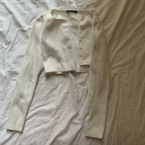 Vit croppad kofta från brandy Melville  - Säljer en stilren vit croppad kofta från  Brandy Melville. Den har långa ärmar och knappar framtill. Perfekt för lager-på-lager-stil eller som ett lättare plagg under svalare dagar.( ai). Men den är One Size från Brandy Melville, passar xs och S!