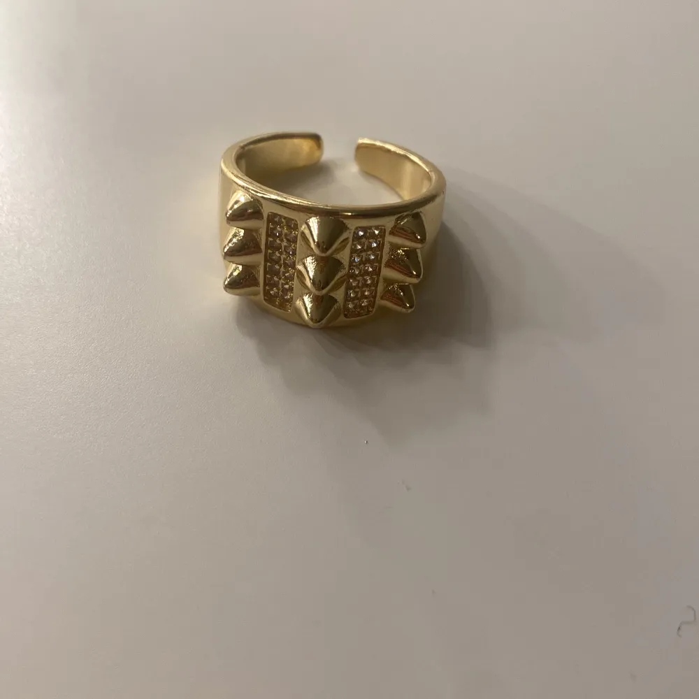 Snygg guldfärgad ring med nitar och glittrande stenar. Ringen har en öppen design vilket gör den justerbar i storlek. Passar med många ringar tveka inte köp!!! ❤️. Asusteet.