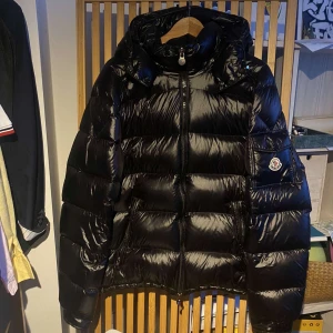 Svart pufferjacka från Moncler - Säljer en snygg svart pufferjacka från Moncler. Jackan har en glansig finish och är utrustad med dragkedja och huva. Perfekt för kyliga dagar när du vill hålla stilen.Moncler jacka  Storlek XL Inga defekter  Knappt använd Djur och rökfritt hem   Skriv gärna om du har frågor!