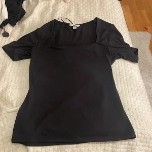 Svart kortärmad topp - Säljer en stilren svart topp med korta ärmar. Perfekt för en enkel och elegant look. Toppen har en mjuk och följsam passform. 